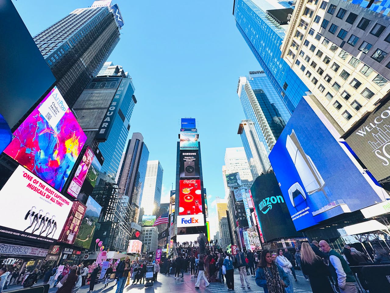 Vibrant daytime view of Times Square, showcasing iconic billboards and bustling crowd in New York City.